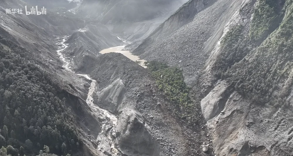 Aerial view of a Himalayan valley filled with grey debris after the mudslide, a muddy barrier lake pooled at its center